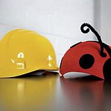 Zwei Faschingshüte für Kinder liegen auf dem Tisch: ein Bauarbeiterhelm liegt links von einem Kinderhut, der das Aussehen eines Marienkäfers hat.
