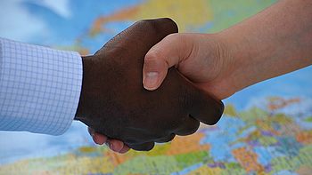 Hände unterschiedlicher Hautfarbe reichen sich die Hände über einer Weltkarte
